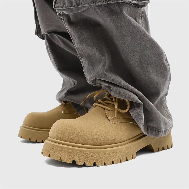 Tan work boots with thick soles worn with gray pants on a light gray background
