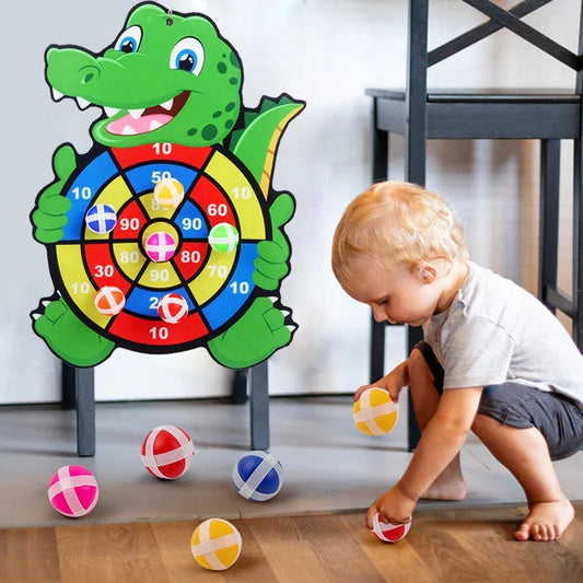 Child playing with a toy dartboard shaped like a crocodile on a wooden floor.