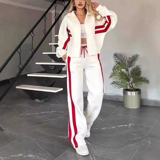 Woman wearing a white and red tracksuit standing in a modern interior setting with a plant.