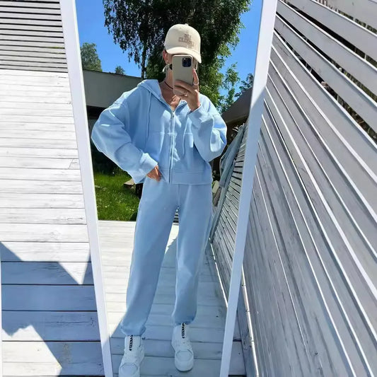 Person wearing a light blue tracksuit taking a mirror selfie on a wooden deck.