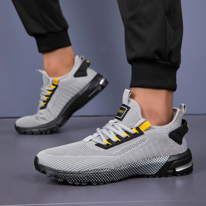 Gray athletic shoes with black and yellow accents worn by a person on a gray background