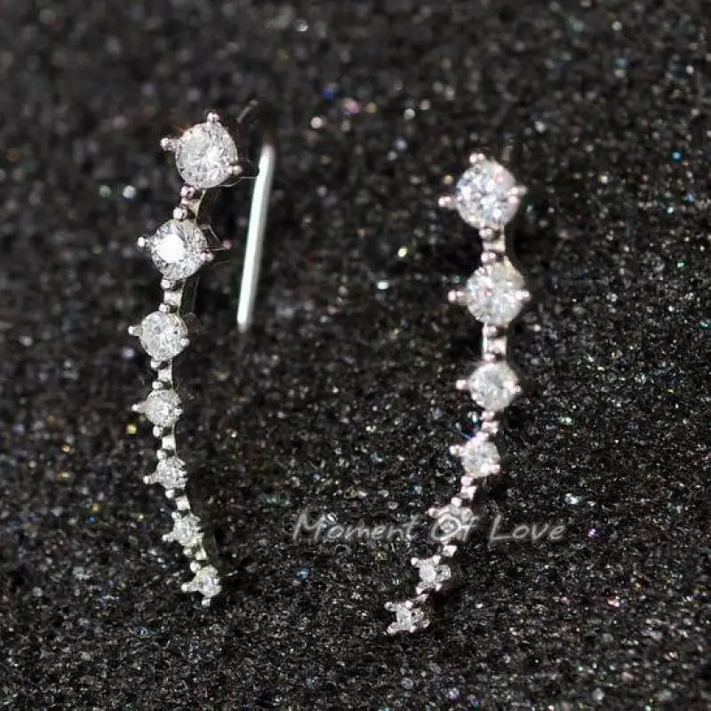 Diamond earrings on a black sand background with 'Moment of Love' branding.