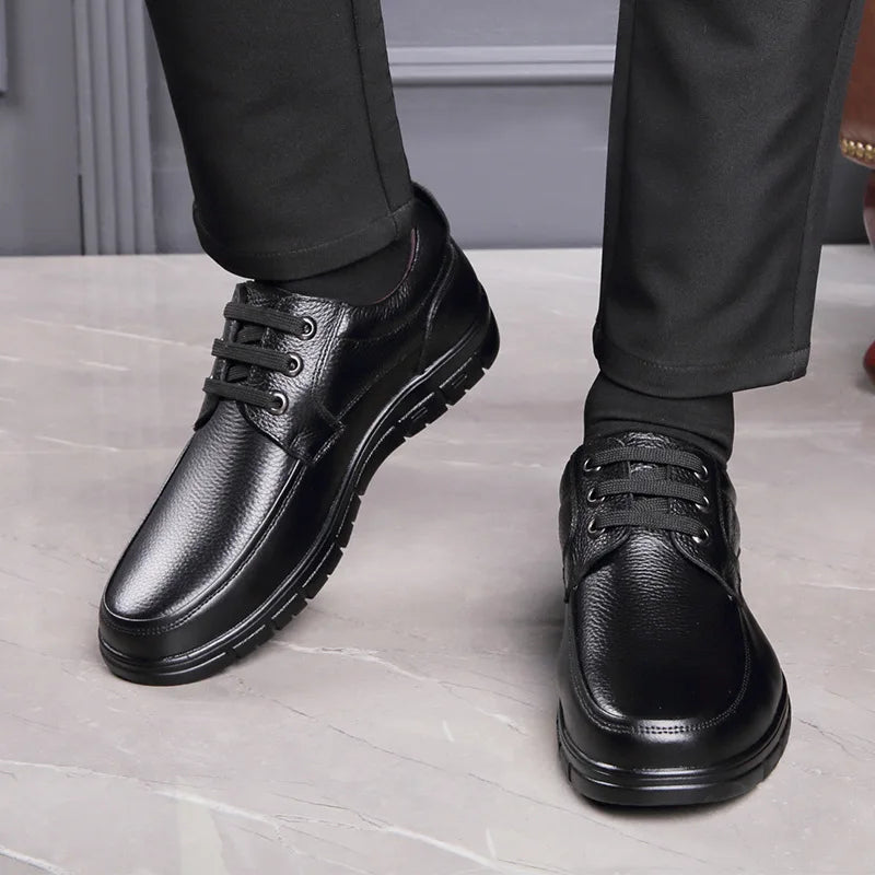 Black leather shoes worn with black pants on a light gray floor.