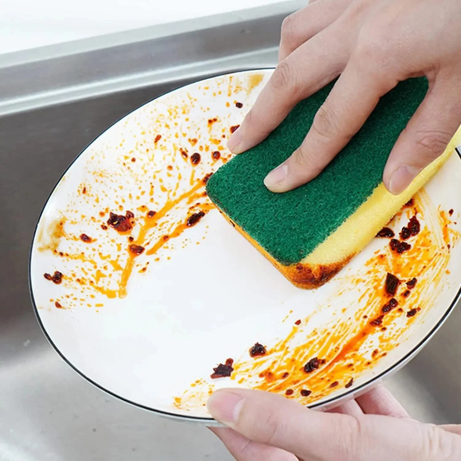 Person cleaning a plate with a green sponge in a kitchen setting