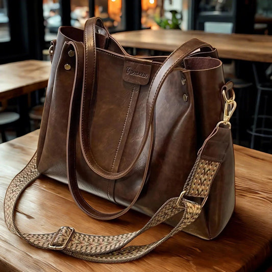 Brown leather handbag with a woven strap on a wooden table.