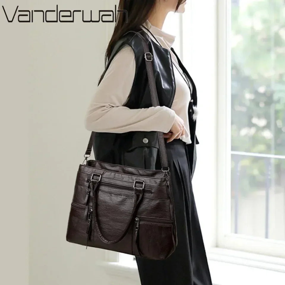 Woman holding a dark brown leather handbag indoors with 'Vanderwalt' branding.