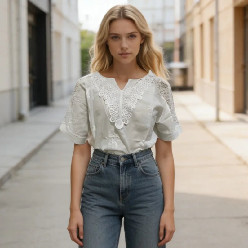 Woman wearing a white blouse with lace details and blue jeans on a city street.