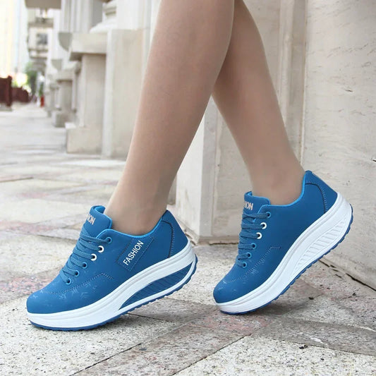 Blue sneakers with white soles worn by a person on a stone pavement.
