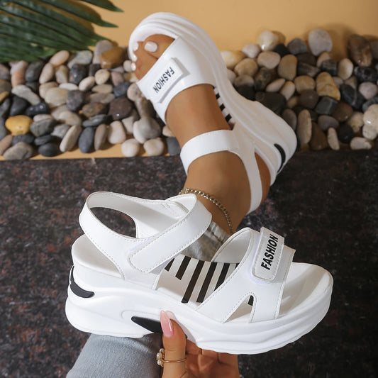 White sandals with 'Fashion' text held by a person against a stone background