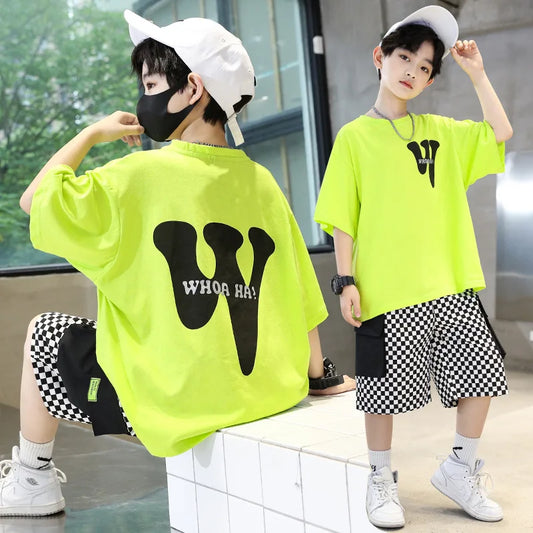 Two children wearing bright green t-shirts with black text and checkered shorts indoors.