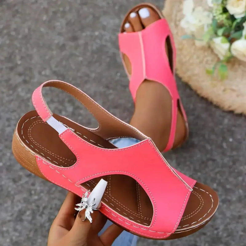 Pink sandals with brown soles held by a hand on a textured surface.