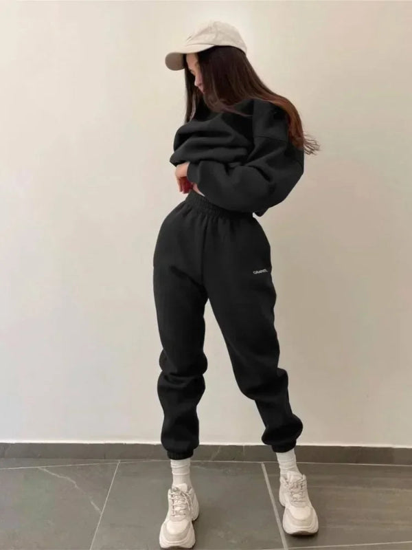Person wearing a black tracksuit and white sneakers against a plain background