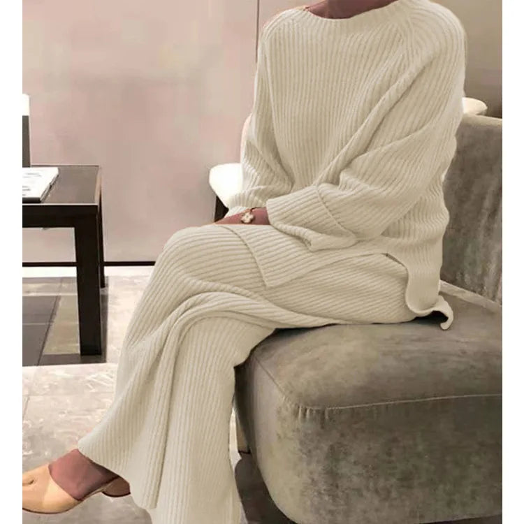 Person wearing a cream ribbed sweater and pants sitting on a gray chair.