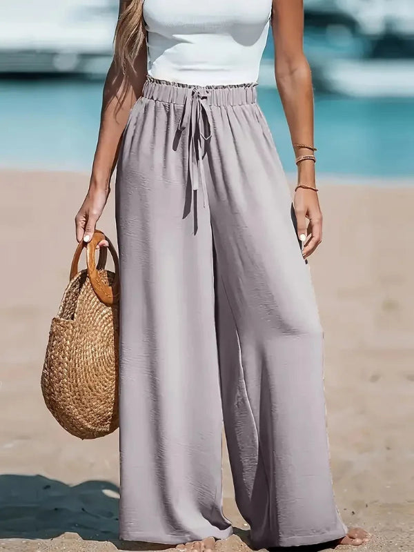 Person wearing light gray wide-leg pants and a white top on a beach.