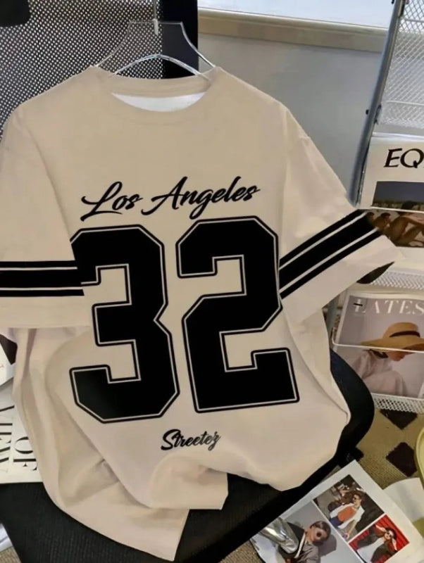 Beige sweatshirt with 'Los Angeles 32' printed on it, hanging against a magazine background.