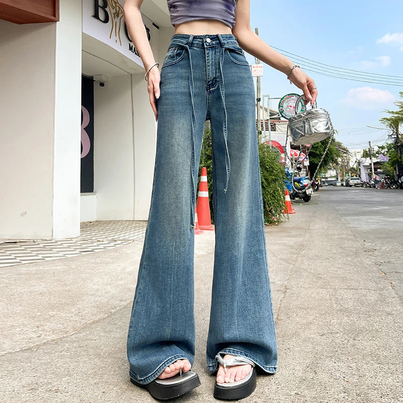 Person wearing blue flared jeans on a street with traffic cones and buildings in the background.