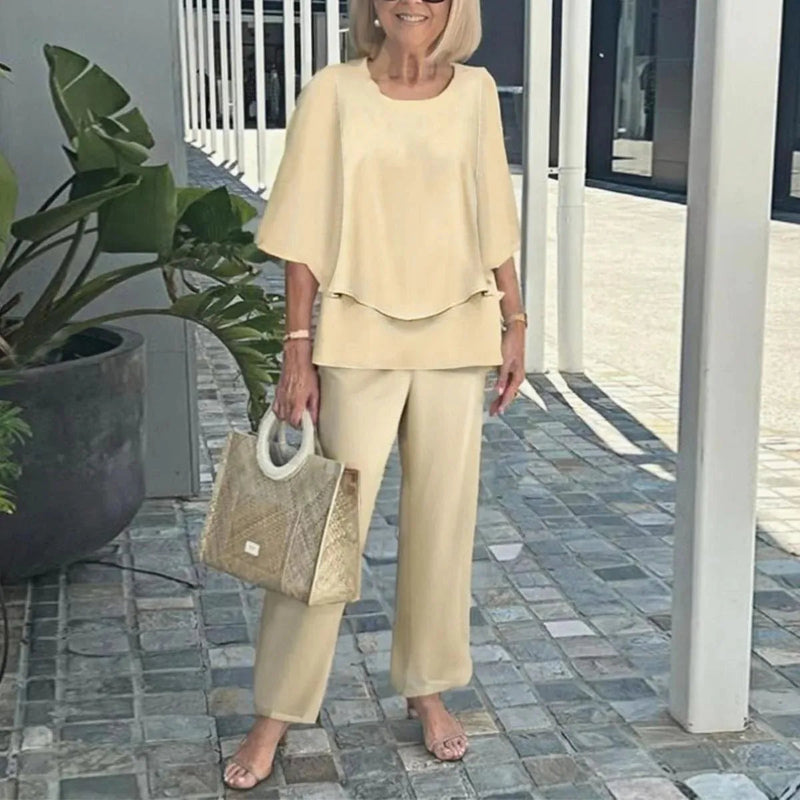 Woman in a beige outfit holding a matching handbag outdoors.