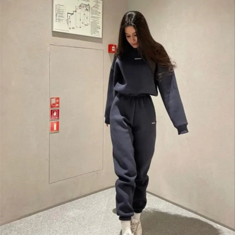 Person wearing a dark blue tracksuit standing in an indoor setting with beige walls and floor.
