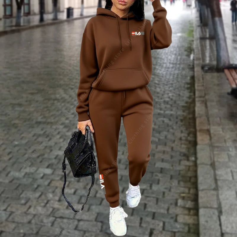 Person wearing a brown tracksuit with a logo, holding a black bag on a city street.