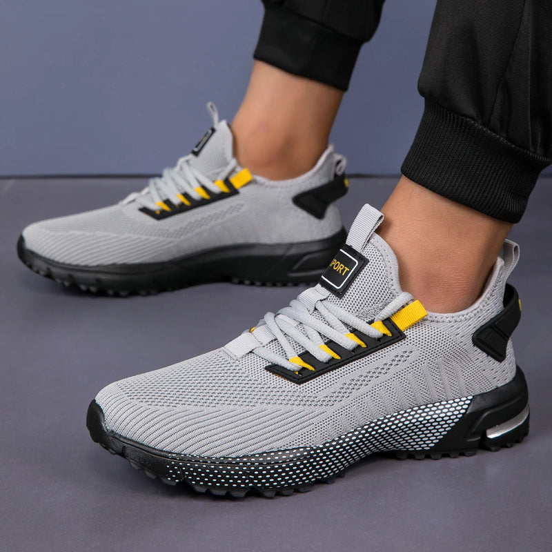 Gray athletic shoes with yellow accents worn by a person on a gray background