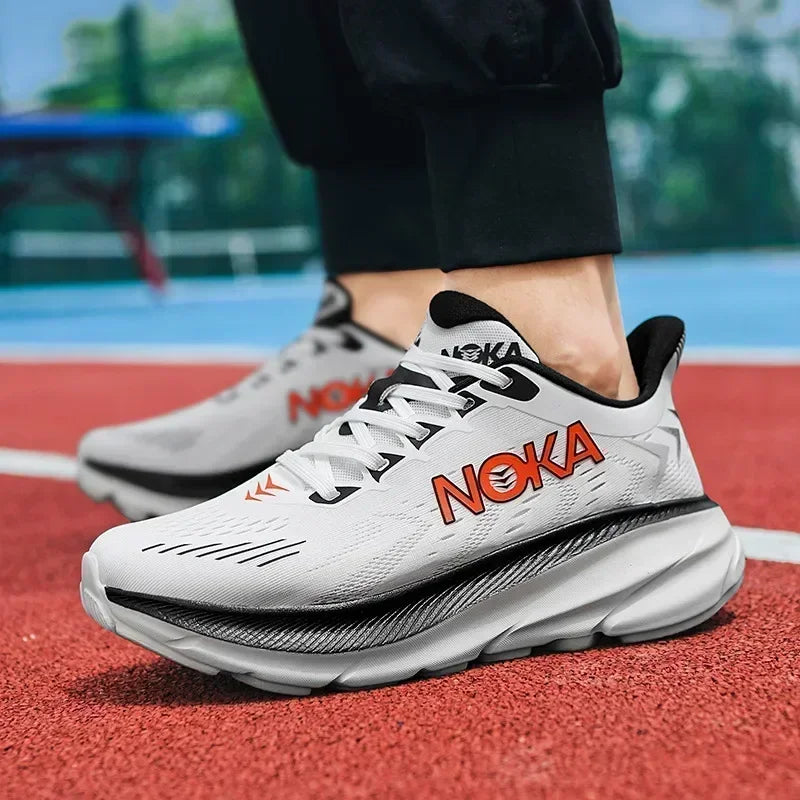 White running shoes with black and orange 'Noka' branding on a red track.