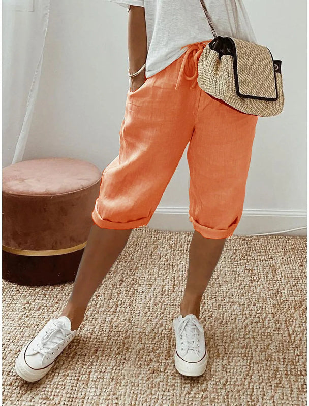 Person wearing orange pants and white sneakers with a straw bag indoors.