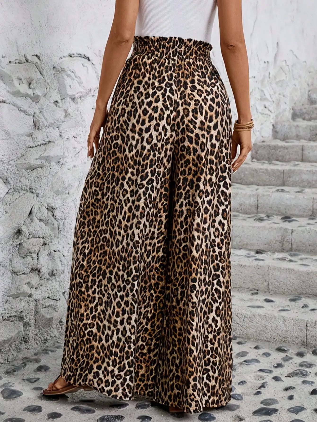 Person wearing leopard print pants standing on a stone path with a white wall background