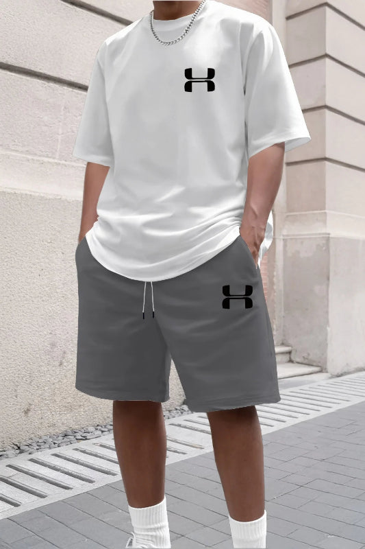 Person wearing a white t-shirt and gray shorts with Under Armour logos, standing against a stone wall.