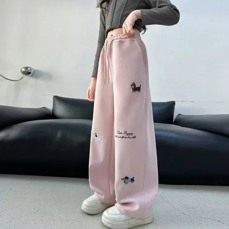 Person wearing pink sweatpants with embroidery designs in a casual setting.