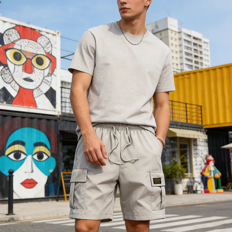 Man wearing a gray t-shirt and cargo shorts standing in an urban setting with colorful murals.