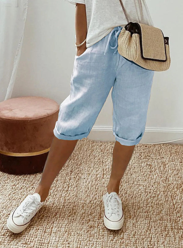 Person wearing light blue shorts, white sneakers, and a straw bag indoors.
