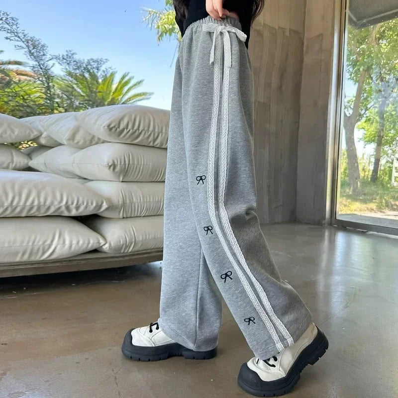 Person wearing gray sweatpants with a brand logo, standing indoors with a concrete floor and stacked pillows in the background.
