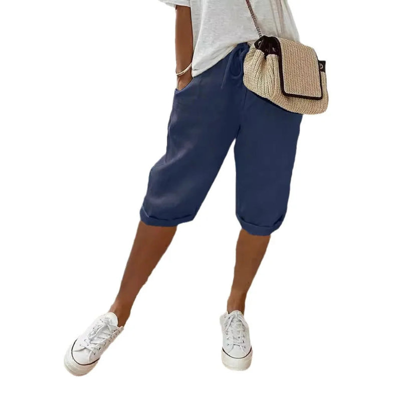 Person wearing blue shorts, white sneakers, and a beige bag on a white background