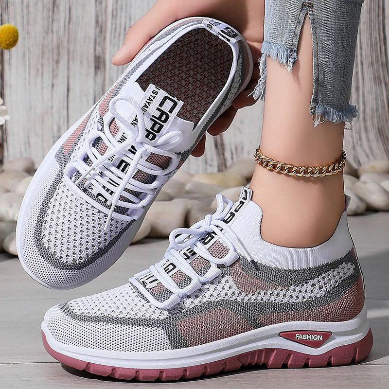 White and gray sneakers with red soles worn by a person on a wooden floor.