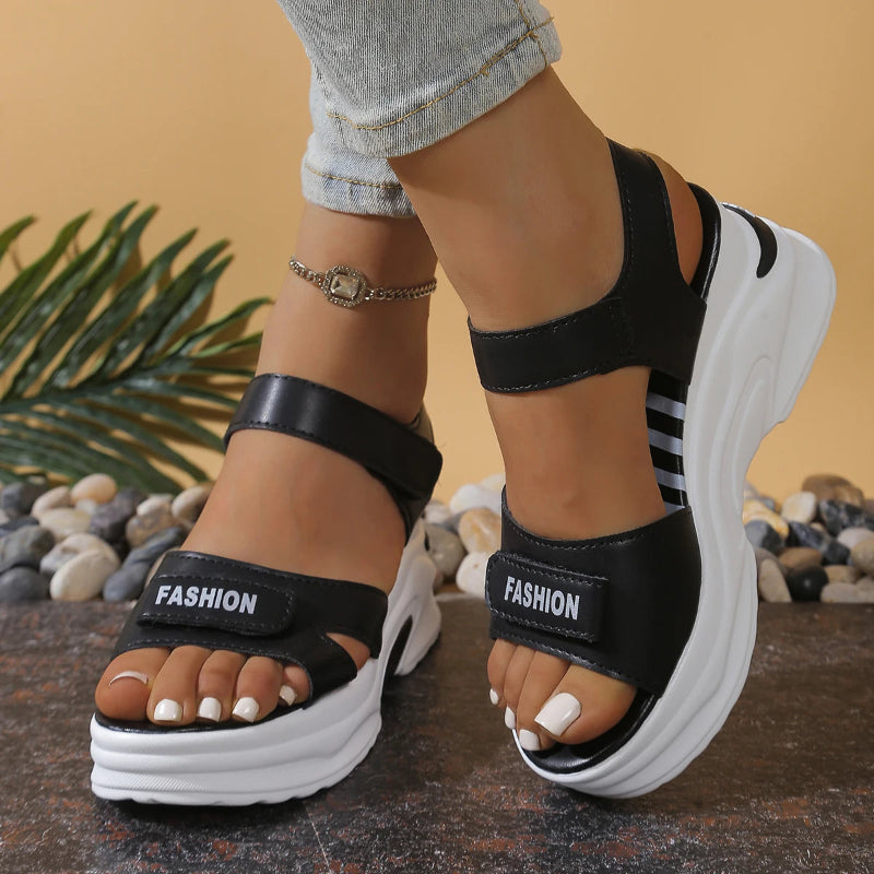 Black platform sandals with 'FASHION' label worn by a person on a neutral background