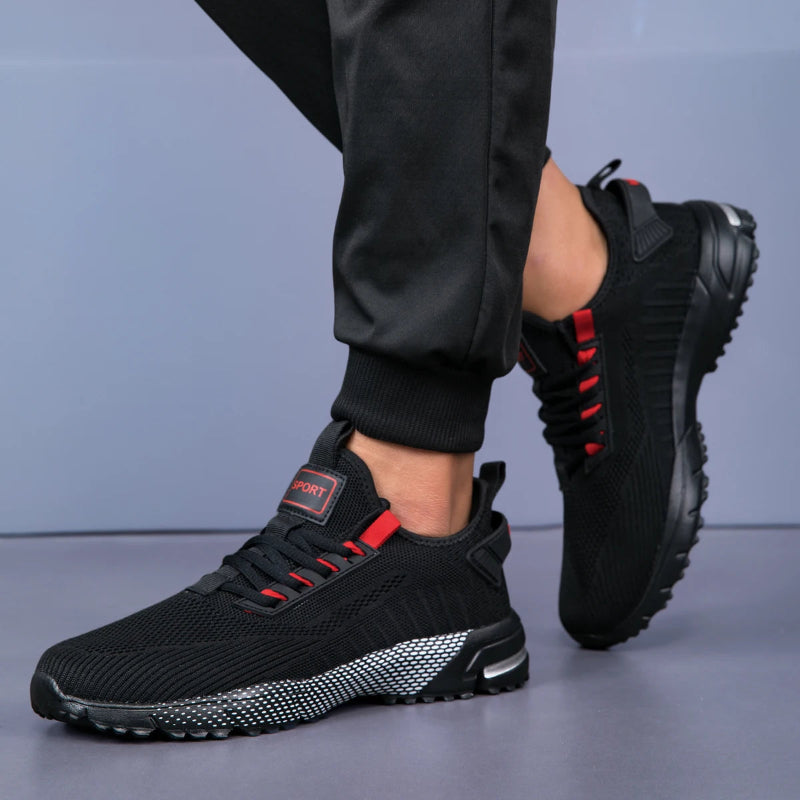 Black athletic shoes with red accents worn by a person on a gray background