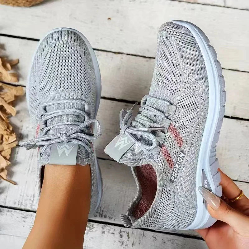 Gray athletic shoes with white soles held by a hand on a wooden floor.