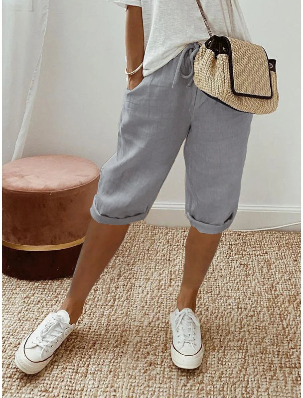Person wearing gray shorts, white sneakers, and a straw bag on a beige carpet.