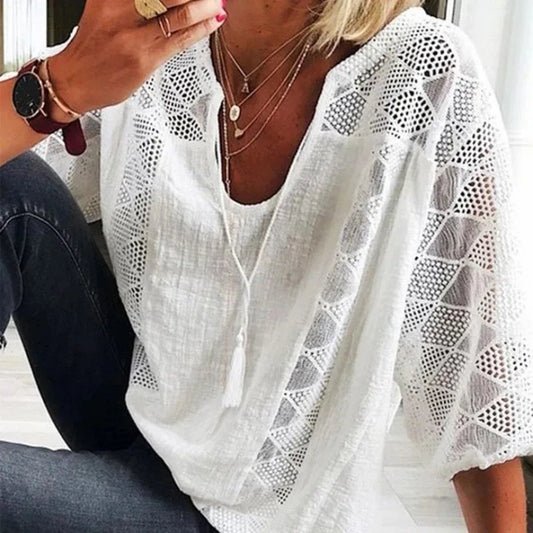 Person wearing a white lace top with geometric patterns, sitting indoors.