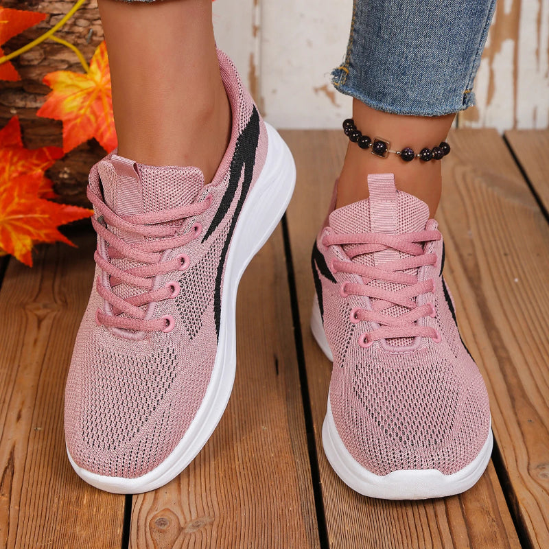 Pink sneakers worn on a wooden floor with autumn leaves in the background