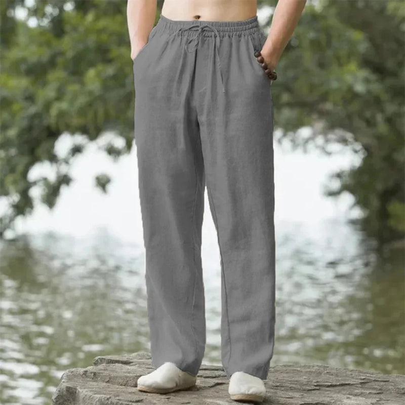 Person wearing gray pants standing by a body of water with trees in the background
