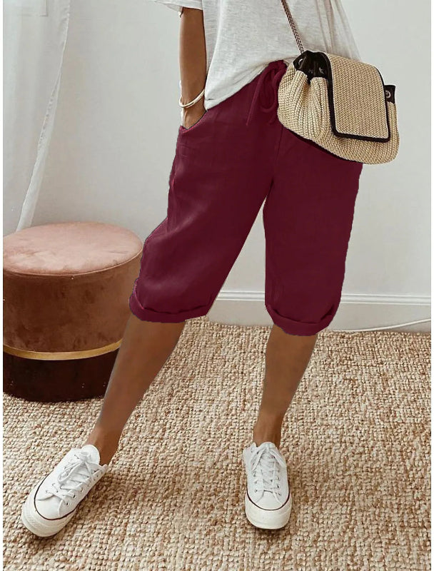 Person wearing maroon shorts, white sneakers, and a straw bag indoors.