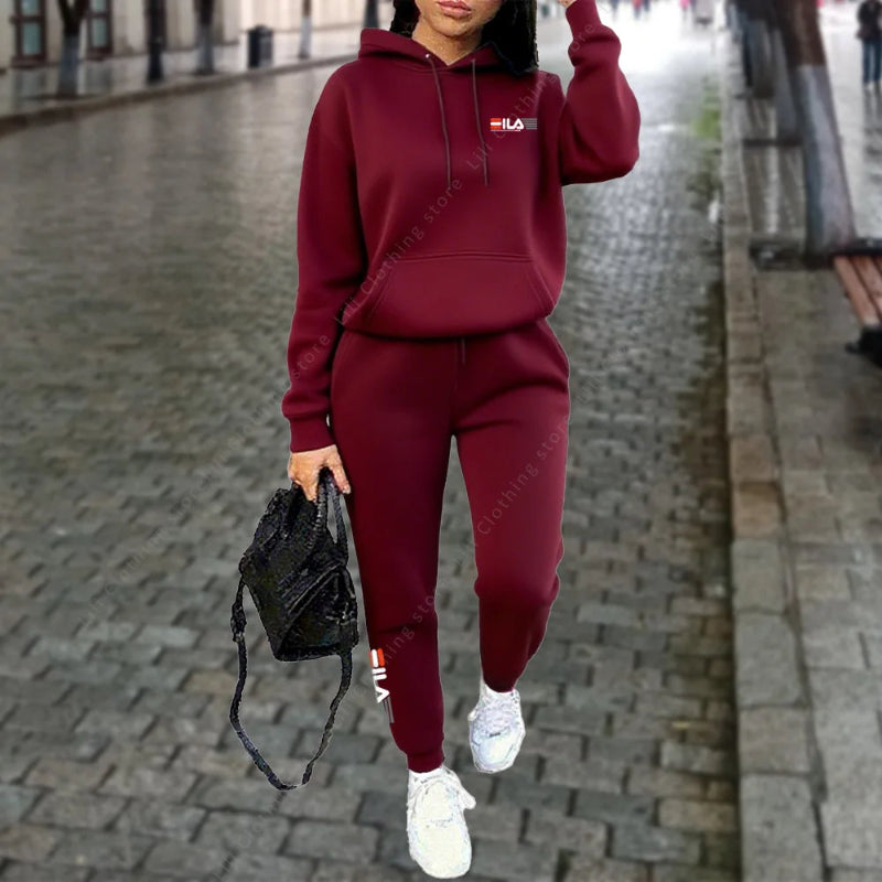 Person wearing a maroon hoodie and pants with a logo, holding a black bag on a street.