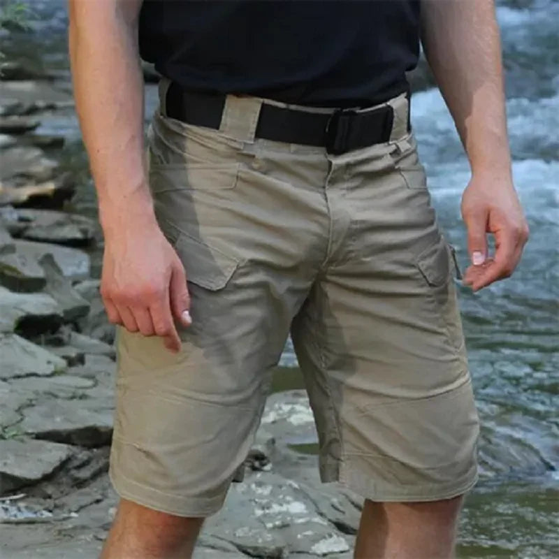 Person wearing beige shorts with a black belt standing near water and rocks.