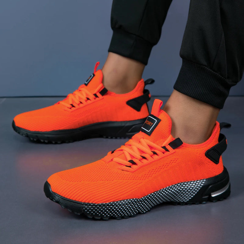 Orange athletic shoes with black accents worn by a person on a gray surface.