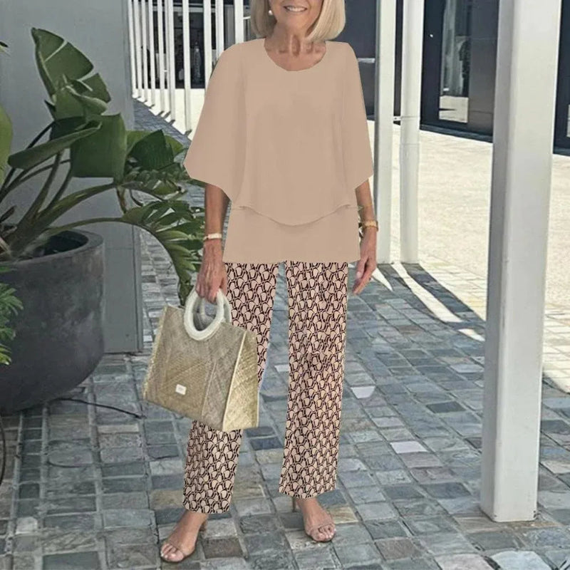 Woman in beige top and patterned pants holding a textured handbag outdoors.