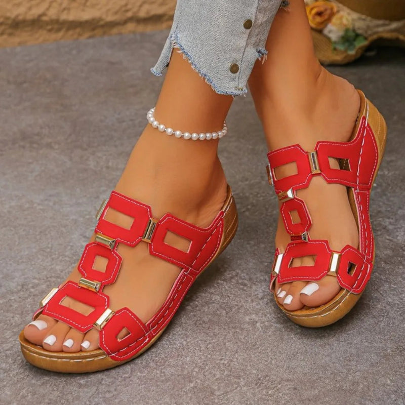 Red sandals with gold accents worn by a person on a gray surface.