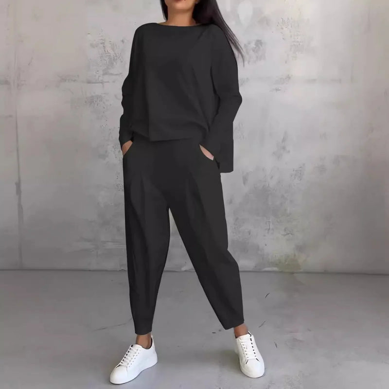 Person wearing a black outfit with white sneakers against a gray concrete wall.